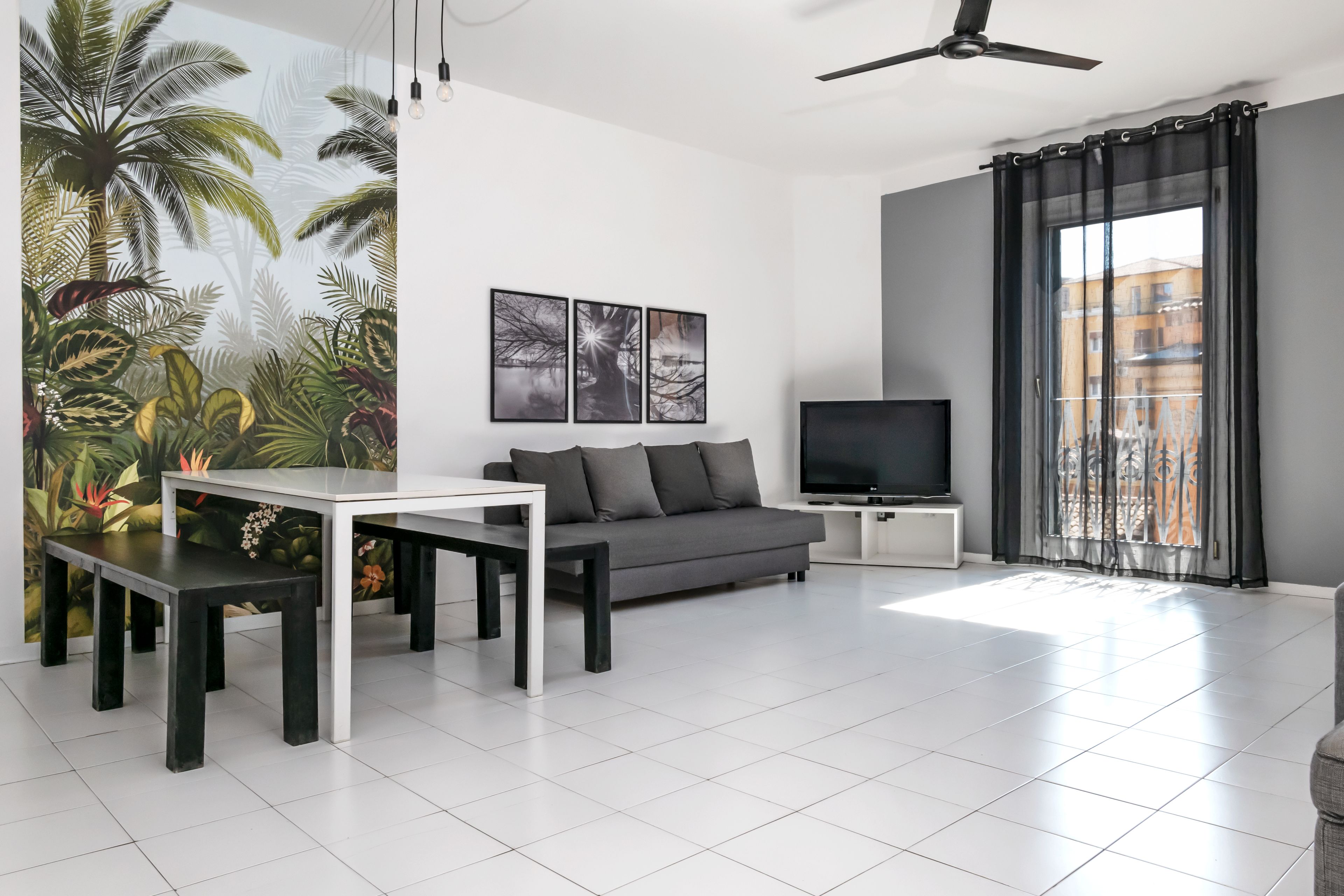 Uma sala de estar moderna com sofá, televisão, mesa de jantar e uma grande janela com cortinas.