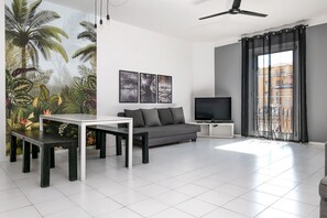 A modern living room with a sofa, a TV, a dining table, and a large window with curtains.