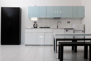 Une cuisine moderne avec des meubles blancs, un réfrigérateur noir, une cuisinière à gaz et une machine à café.