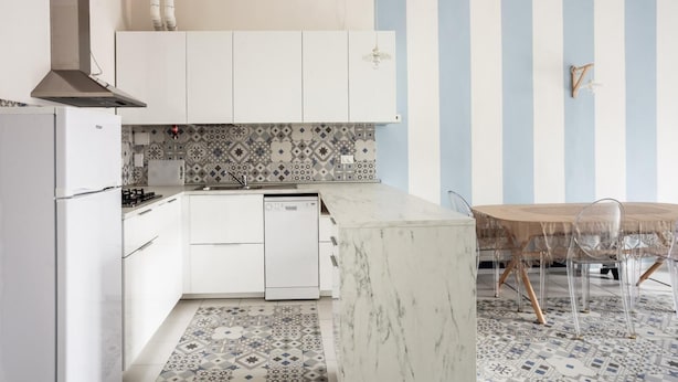Una cocina moderna con armarios blancos, una isla de mármol y un salpicadero con diseño.