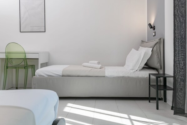 A modern bedroom with a bed, a desk, a chair, and a bedside table.