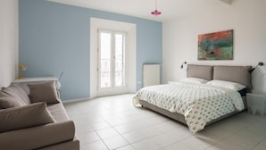 Un dormitorio con cama, sofá, radiador, ventana y un cuadro en la pared.
