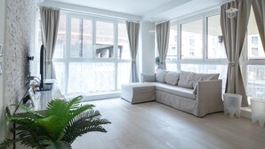 A modern living room with a large window, a white sofa, a flat-screen TV, and a potted plant.