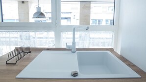 A modern kitchen with a white sink, a pendant light, and a window with lace curtains.