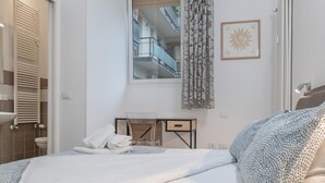 Een slaapkamer met een bed, een nachtkastje met een lamp, een raam met gordijnen en een uitzicht op een gebouw.