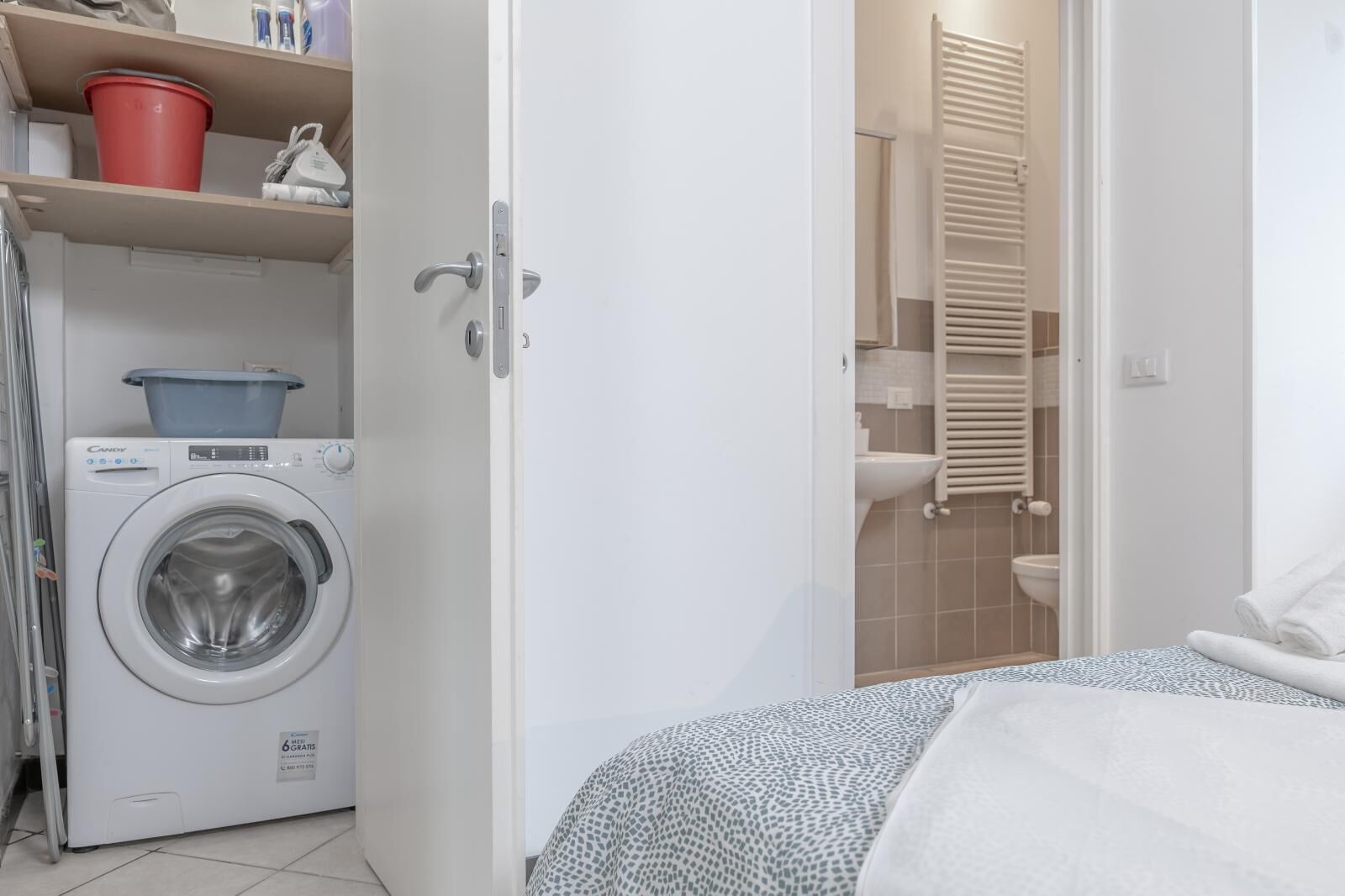 A laundry area with a washing machine, a red bucket, and a towel rack.