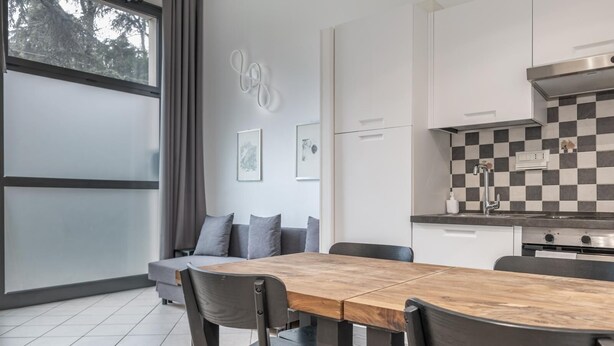 Een moderne keuken met een geruit spatwand, een eettafel met stoelen en een grijze bank met kussens.