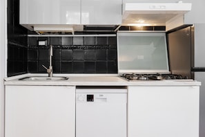 Een keuken met een vaatwasser, fornuis en een zwart betegelde achterwand.