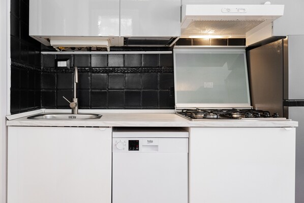 Una cocina con lavavajillas, estufa y un salpicadero de azulejos negros.