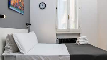 A neatly made bed with white linens, a black headboard, and a grey blanket. There is a wall clock and a painting above the bed.