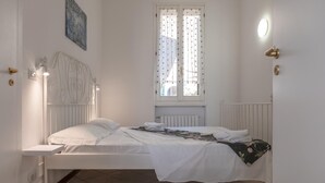Een slaapkamer met een bed, een raam met gordijnen, een radiator en een wandlamp.