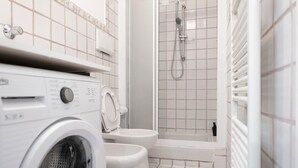 Een wasruimte met een wasmachine en droger, een toilet en een douche.
