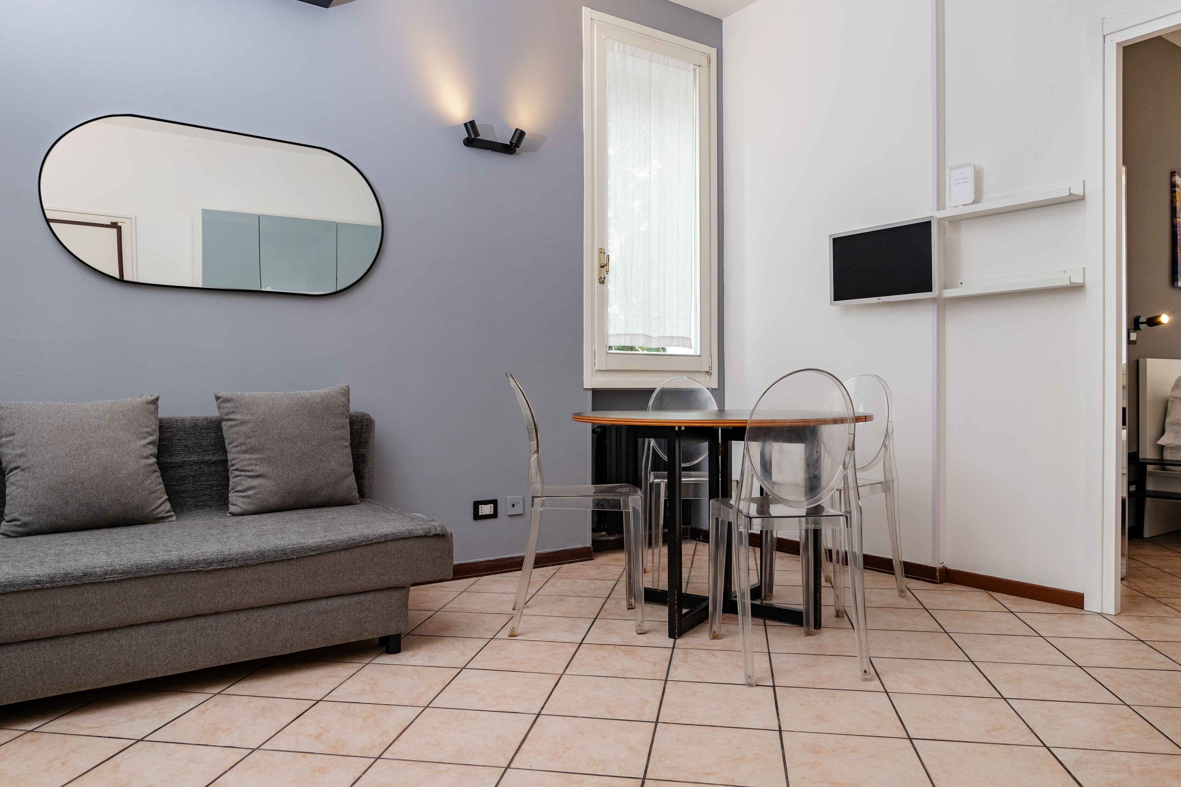 A modern living room with a grey sofa, a round table, and clear chairs.