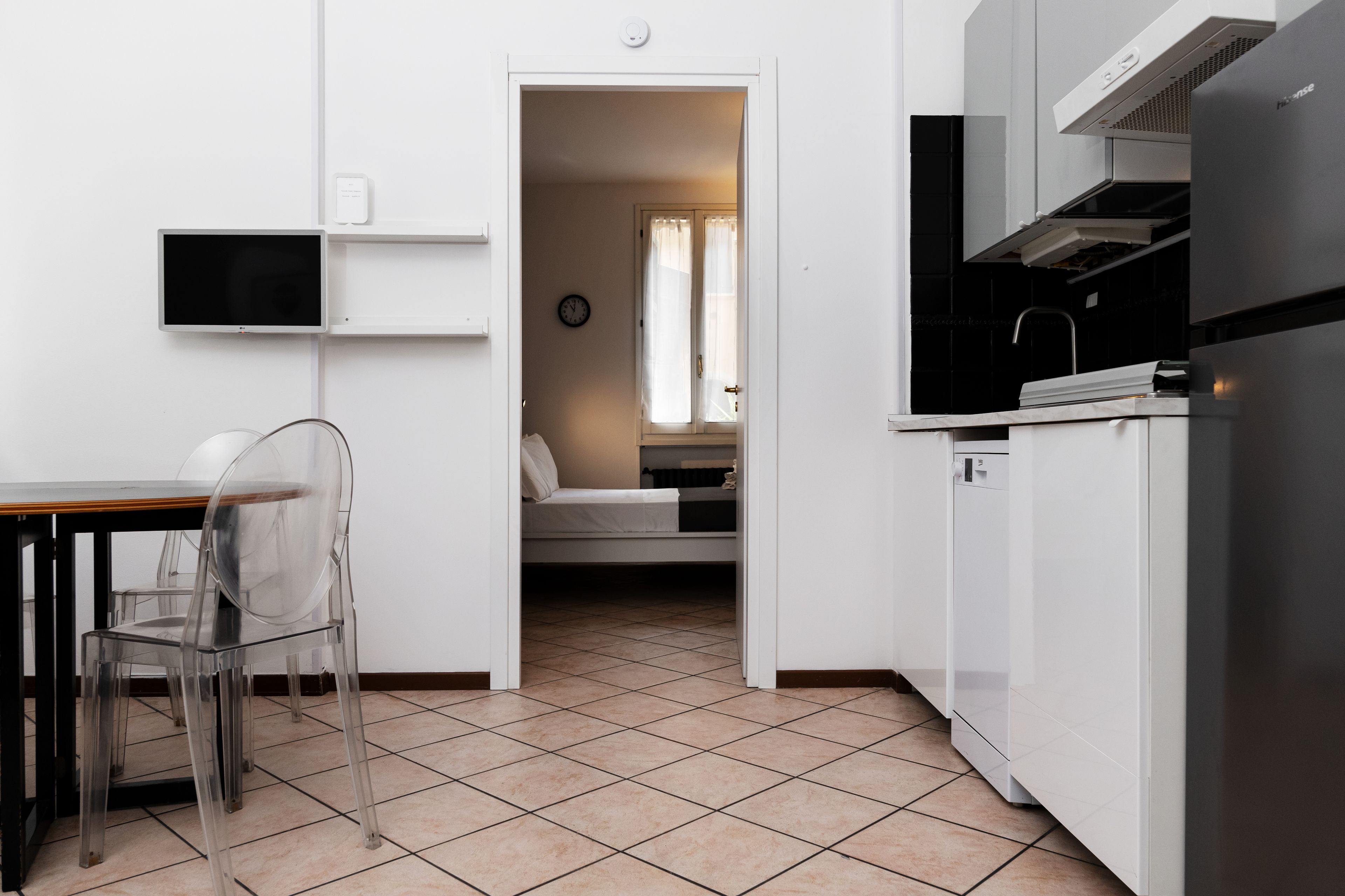 A compact kitchen with a dining area, a built-in TV, and a visible bedroom with a bed and curtains.