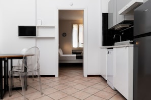 Cocina compacta con comedor, televisor integrado y dormitorio visible con cama y cortinas.