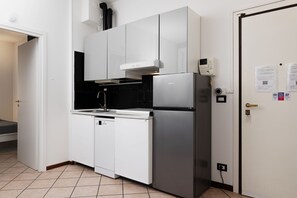 Cocina compacta con alacenas blancas, refrigerador de acero inoxidable y salpicadero de azulejos negros.