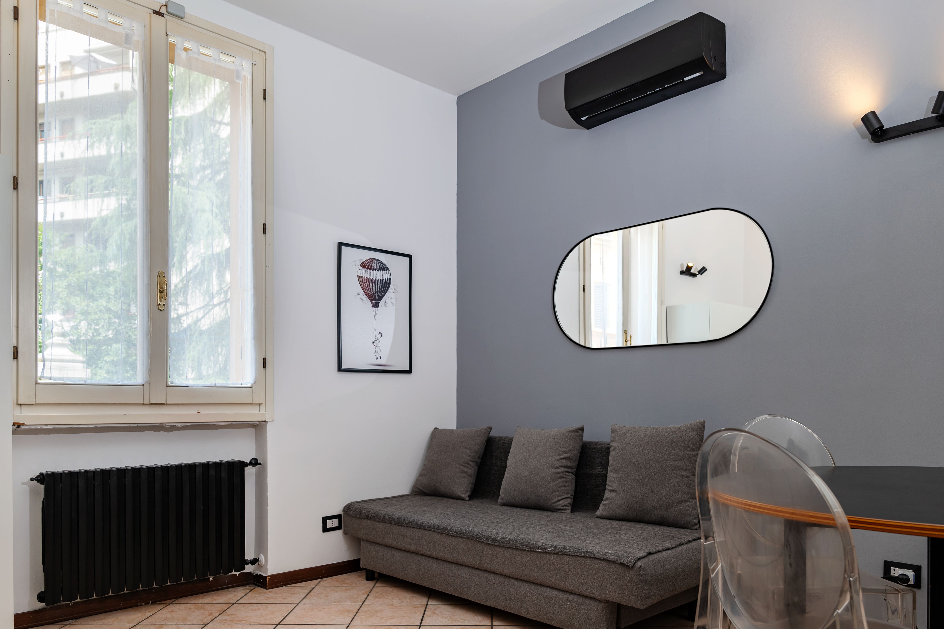 A modern living room with a grey sofa, a framed picture, a wall-mounted mirror, and a radiator.