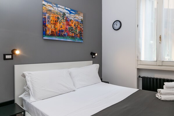 Una habitación de hotel con una cama, un cuadro en la pared, un reloj y una ventana con cortinas.