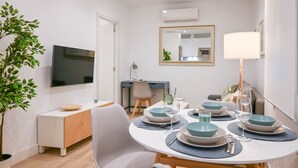 Ein moderner Essbereich mit einem runden Tisch, gedeckt für vier Personen, umgeben von weißen Stühlen. Ein Flachbildfernseher ist an der Wand über dem Tisch angebracht.