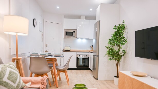 Eine moderne Wohnung mit Essbereich, Küchenzeile und Wohnzimmer mit Fernseher und einer grünen Vase.