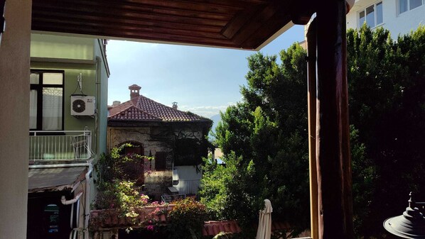 A balcony with a view of a stone building, a fan, and some greenery. - Antalya Inn Hotel (Antalya)