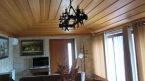 Una stanza con travi a vista in legno, un lampadario, un camino, una televisione e una finestra con tende.