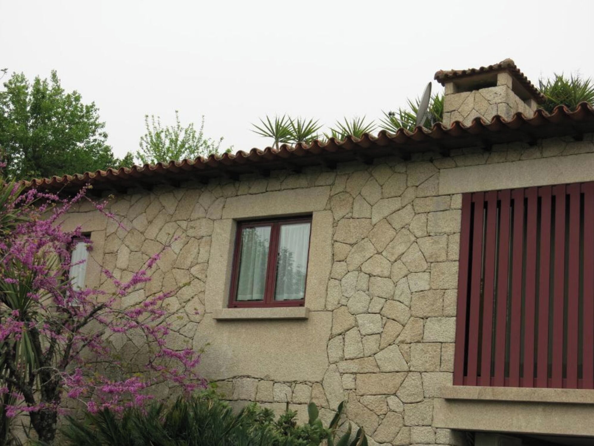 Un edificio in pietra con tetto a tegole, una piccola finestra e un battente rosso.