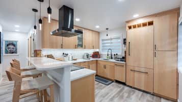 Una cocina moderna con armarios de madera, una isla central, iluminación colgante y un ventanal grande.