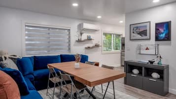 Una sala moderna con un sofá azul, una mesa de comedor de madera y un mueble de almacenamiento gris con estantes.
