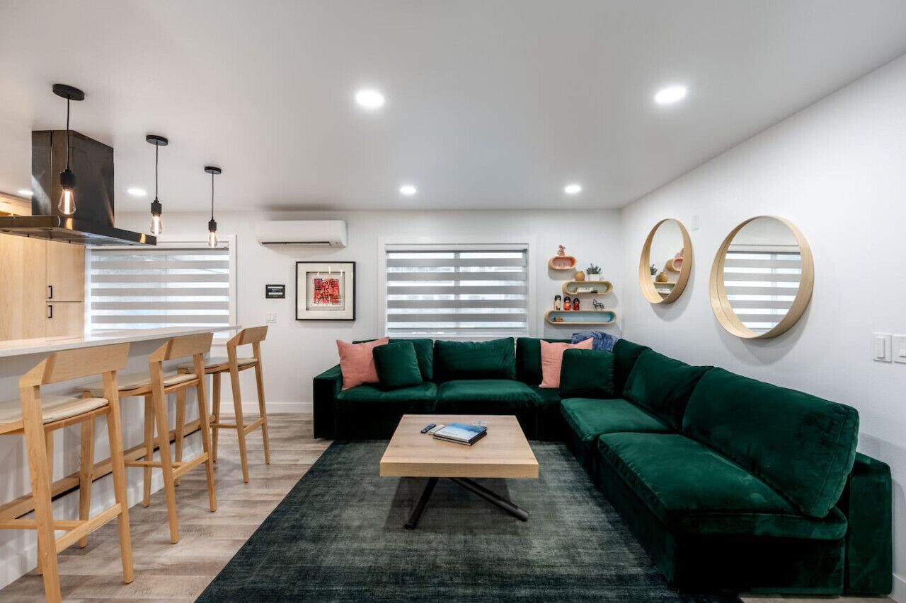 A modern living room with a green sofa, wooden chairs, a coffee table, and a kitchen area with a bar counter.