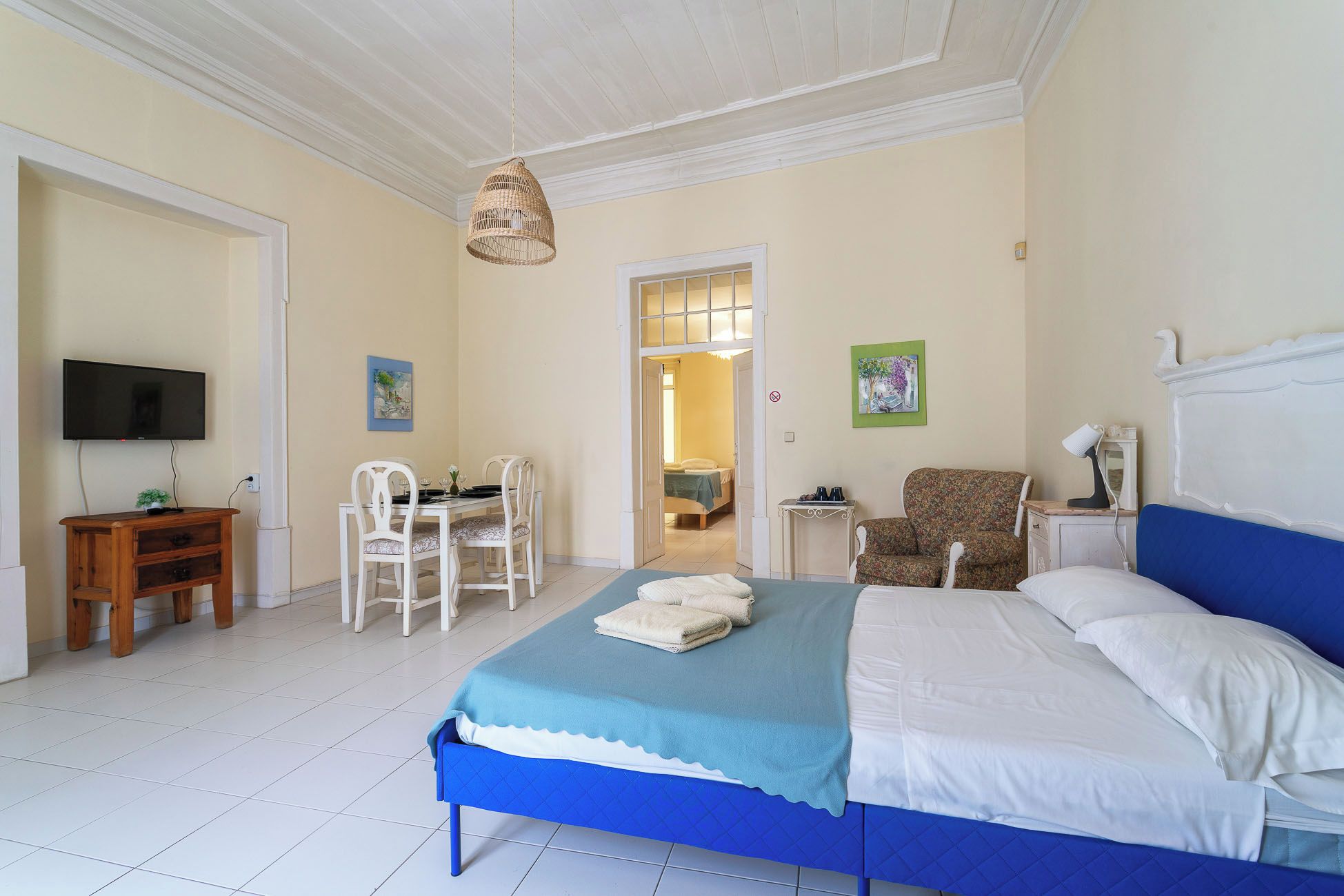Une chambre à coucher comprenant un lit, un bureau, une chaise, un téléviseur et une porte donnant sur une autre pièce.