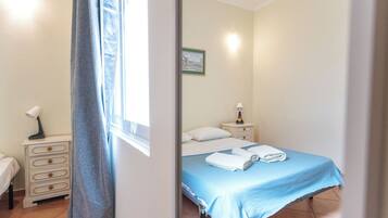 Quarto com cama, mesa de cabeceira, luminária e janela com cortinas.