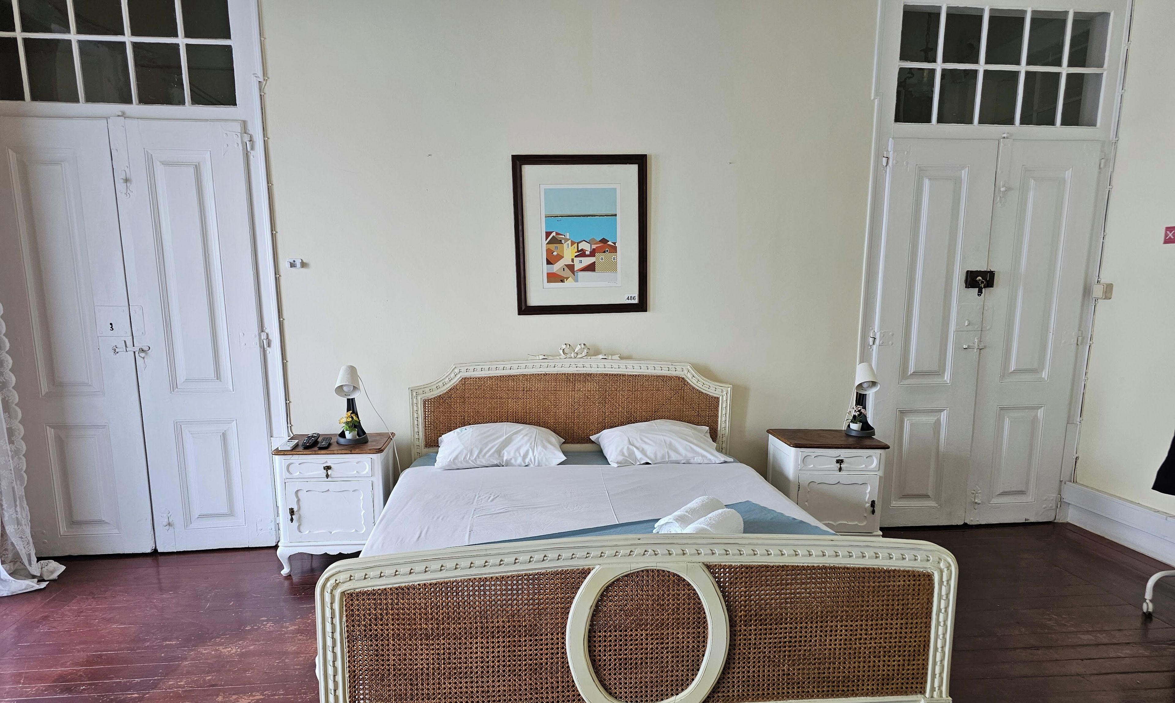 Quarto com uma cama, duas mesas de cabeceira, um quadro na parede e portas brancas.