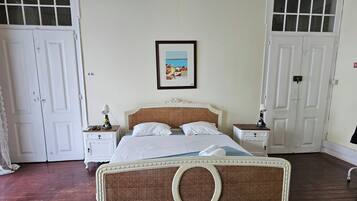 Quarto com uma cama, duas mesas de cabeceira, um quadro na parede e portas brancas.