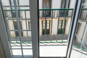 Vista a través de una ventana con una reja de metal, un edificio con puerta verde y suelo empedrado.