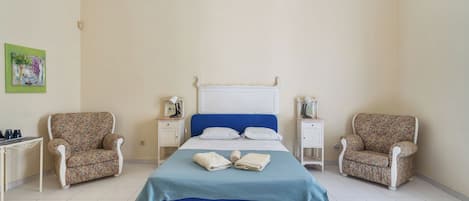 A bedroom with a bed, two nightstands, two chairs, a hanging light fixture, and a painting on the wall.
