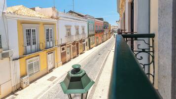 Una calle estrecha flanqueada por edificios, una baranda de metal verde y un cielo despejado.