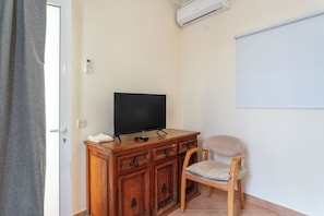 Una habitación con una televisión sobre un mueble de madera, una silla y una pizarra en la pared.