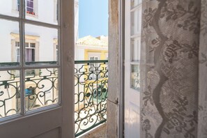 Una ventana con barandilla de metal en el balcón y un cortinaje de encaje medio bajado.