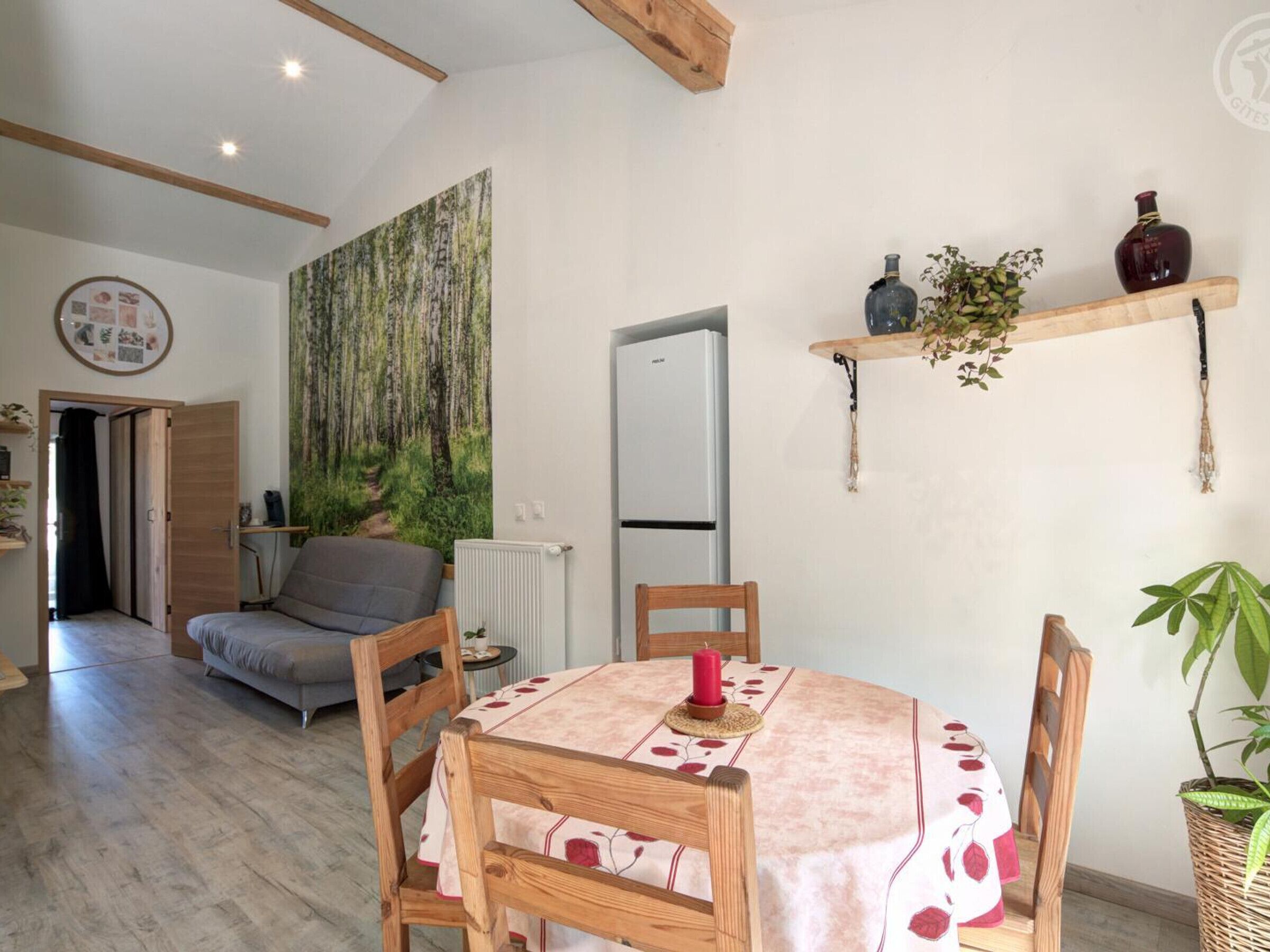 Una sala de estar acogedora con un sofá, una mesa de comedor con sillas, un radiador y un mural grande con motivos forestales.