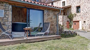 A stone building with a wooden deck, two lounge chairs, and a table with a tray of items. - Two cozy stone cottages for 11 people with optional spa (Saint-Julien-Molin-Molette)