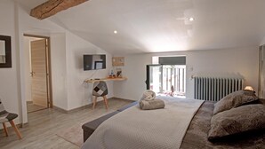 A bedroom with a bed, a chair, a desk, a radiator, and a television. - Two cozy stone cottages for 11 people with optional spa (Saint-Julien-Molin-Molette)