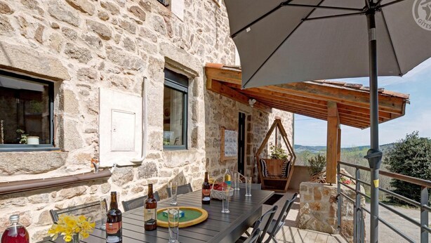 A stone building with a terrace table set for dining, featuring bottles and glasses, and a hanging chair. - Two cozy stone cottages for 11 people with optional spa (Saint-Julien-Molin-Molette)