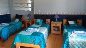 Une chambre d’hôtel avec deux lits simples, chacun recouvert d’une couvre-lit bleue et agrémenté d’oreillers assortis. Il y a deux tables de chevet avec des lampes, et un luminaire fixé au mur au-dessus des lits.