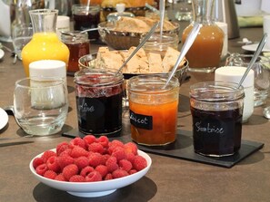 Een buffettafel met diverse etenswaren, waaronder potten jam, een kom frambozen en een glas jus d'orange.
