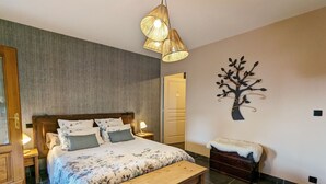Een slaapkamer met een bed, een bankje, een wanddecoratie van een boom en een deur.