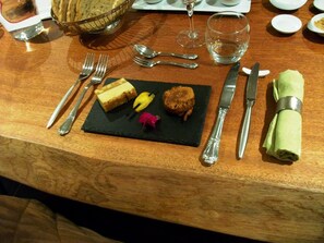 Een houten tafel met een dessertbord met een plakje taart, een koekje en een spiesje fruit.