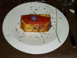 Une assiette sur laquelle est disposé un plat rectangulaire nappé de sauce rouge et décoré d’herbes.