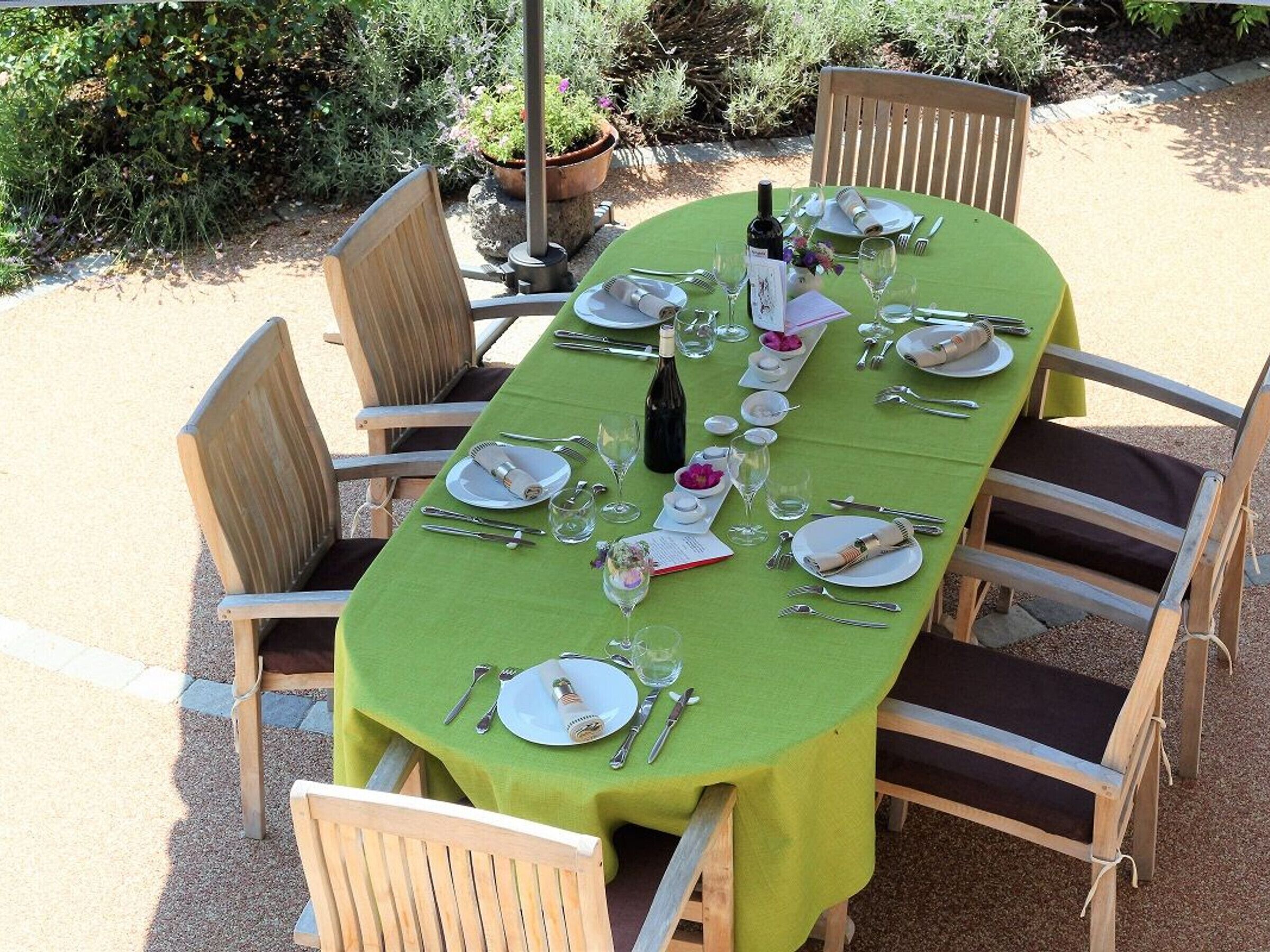 Une table de jardin, avec des chaises, une bouteille de vin, ainsi que différentes assiettes et couverts.