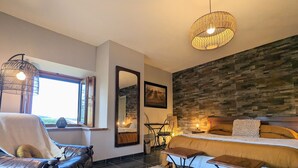 A modern bedroom with a large bed, a leather armchair, a small table, and a stone accent wall. - Spacious suite with wellness, parking, wifi, in Saint-Privat-d'Allier (Saint-Privat-d'Allier)